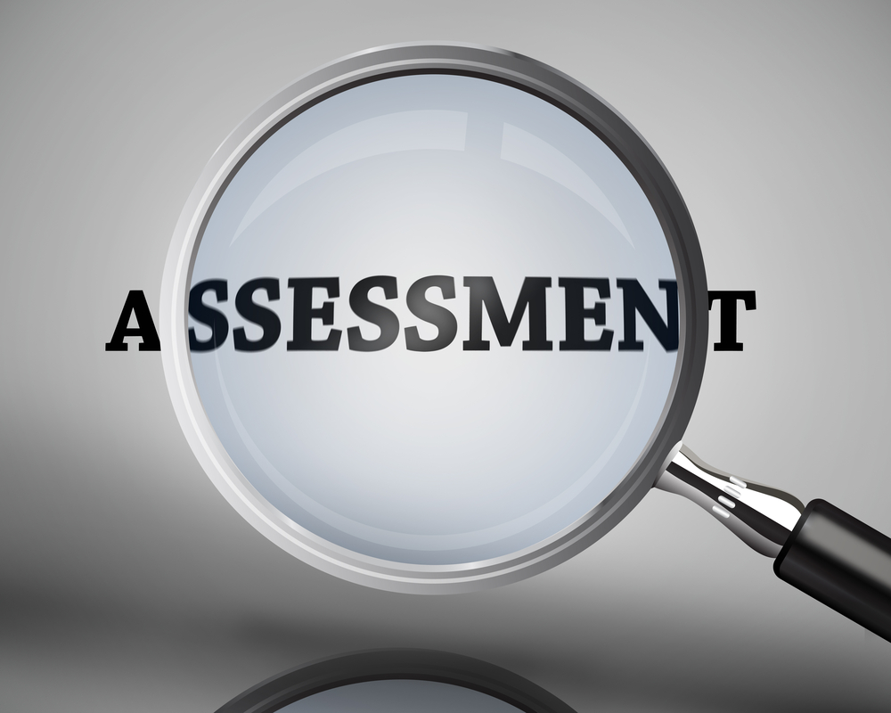 Magnifying glass showing assessment word on grey background Magnifying glass showing assessment word on grey background